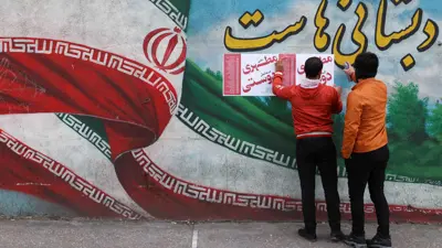 رجال إيرانيون يعلقون ملصقات الحملة الانتخابية 
