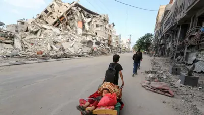 طفل فلسطيني يسحب عربة تحمل شقيقه هربًا من غارات إسرائيلية على قطاع غزة