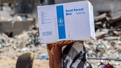 فلسطيني يحمل سلة غذائية من الأونروا