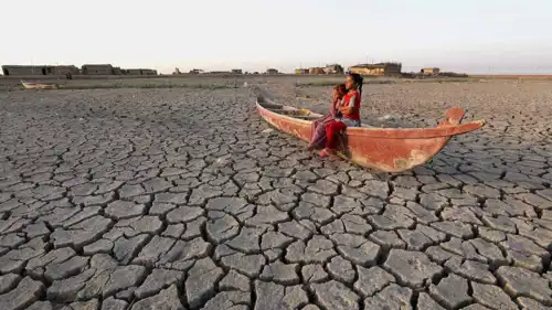 طفلان يجلسان في قارب وسط الجفاف في العراق