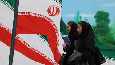  إيرانيات يمررن أمام لوحة جدارية للأعلام الإيرانية في طهران