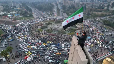  سوري يرفع العلم الجديد في ساحة الأمويين 