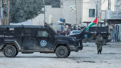 فلسطيني يحمل علم بلاده أمام دورية شرطة في مخيم جنين