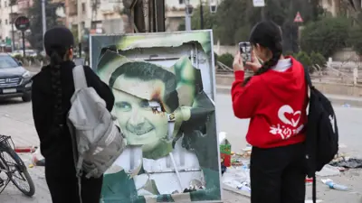 أطفال سوريون أمام صورة ممزقة للرئيس السابق الأسد