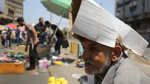 بائع متجول عراقي يحمي رأسه من الشمس باستخدام قطعة من الكرتون
