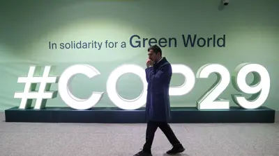رجل يمشي أمام منشأة تحمل الشعار COP29