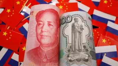 تظهر الأوراق النقدية من اليوان الصيني والروبل الروسي وسط علمي الصين وروسيا 